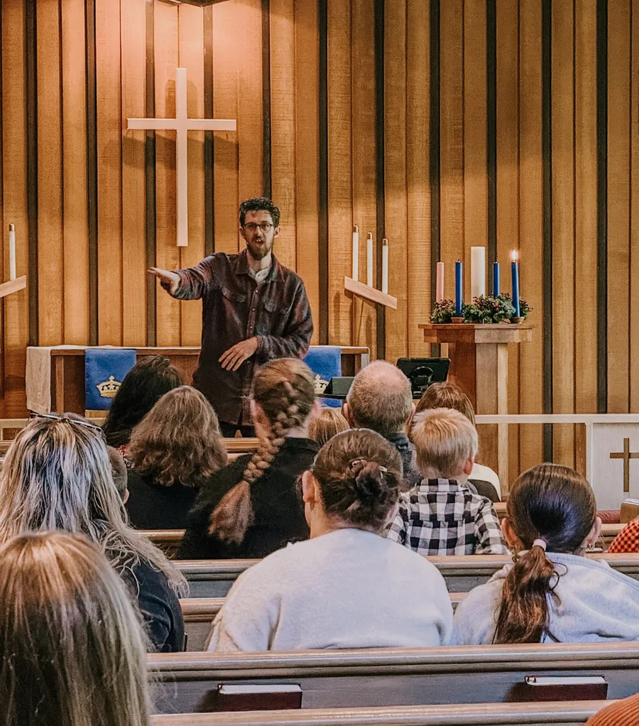 A pastor teaching from a wooden pulpit in front of a seated congregation
