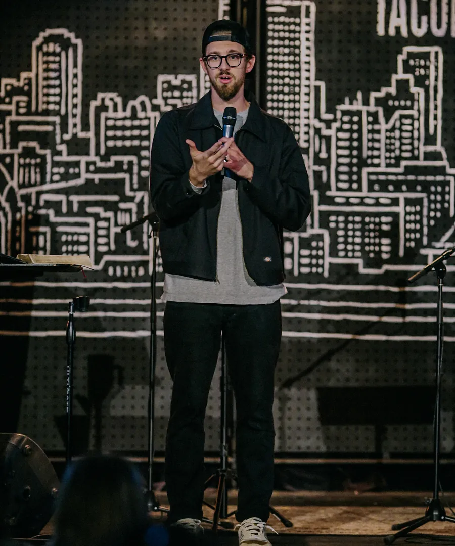 A pastor speaking into a microphone in front of a city skyline backdrop