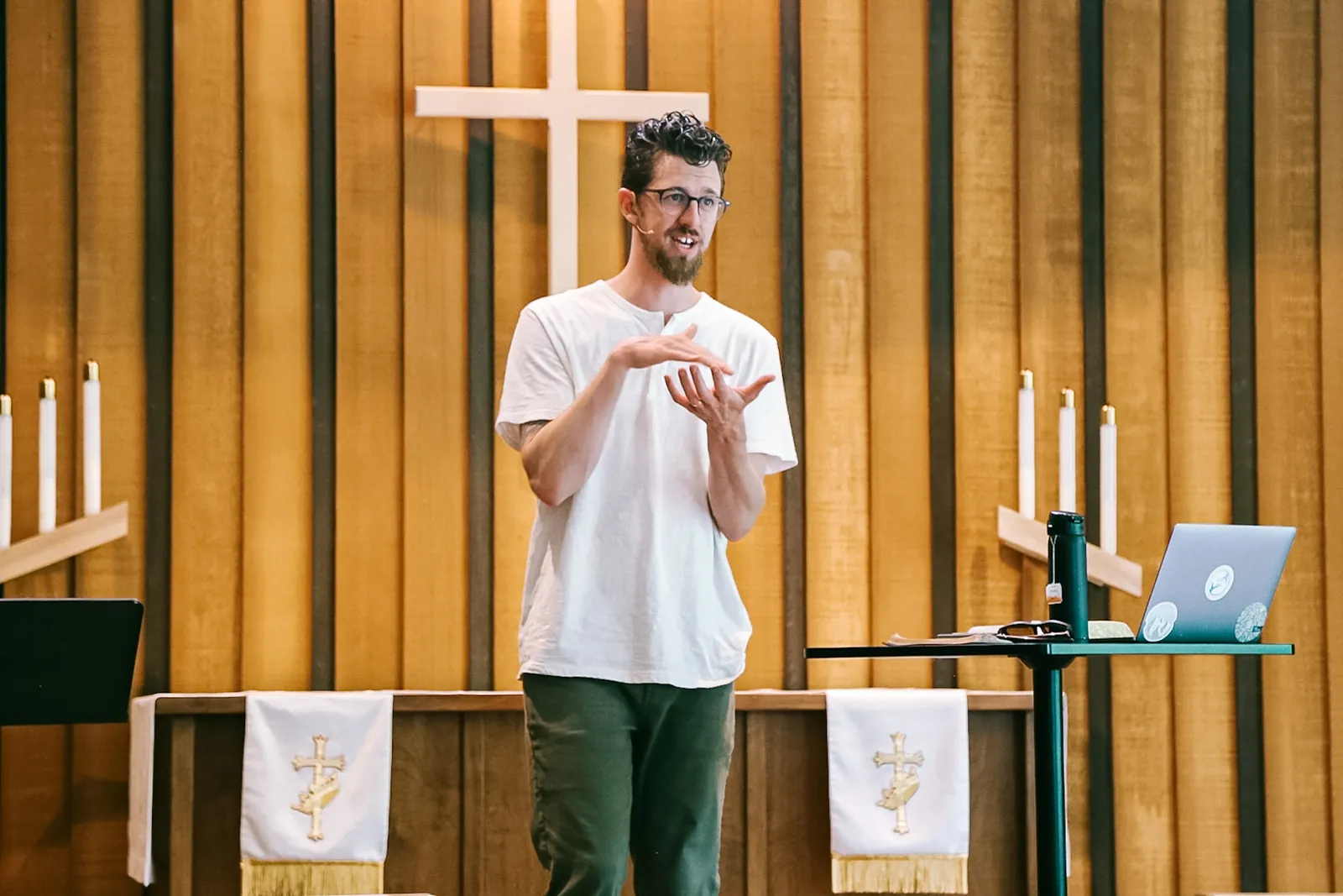 A pastor talking with his hands from a wooden pulpit under a cross